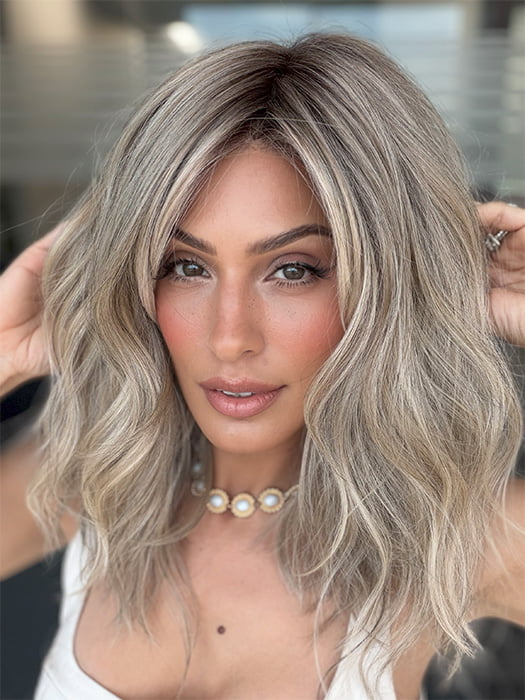 Model is wearing BEACH WAVE MAGIC by TRESSALLURE in color 36/25/23/R6 MOON DUST | Dark salt and pepper base with blended golden blonde and cool platinum tones, shaded with Dark Roots