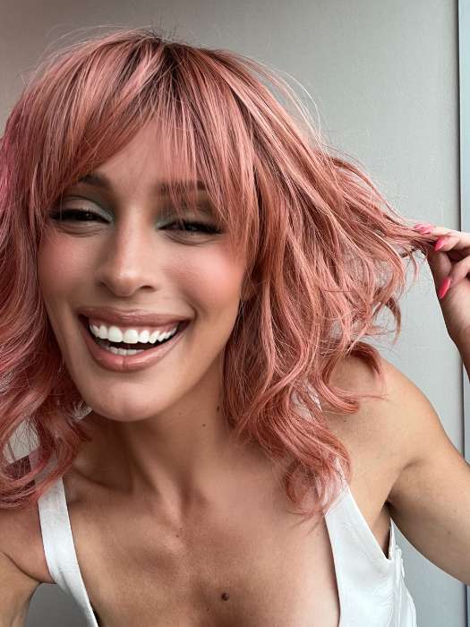 Model is wearing BREEZY WAVEZ by RENE OF PARIS in color DUSTY-ROSE | Medium Coral Red Base with Dark Brown Roots